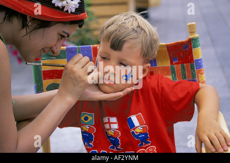 A face painter makes a design on the cheek of a young boy on Canada Day in Old Montreal, Canada. Stock Photo