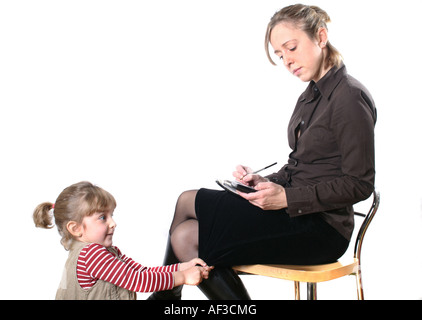 young mother with organizer and mobile phone, typing a SMS while her daughter is pulling at her lap Stock Photo