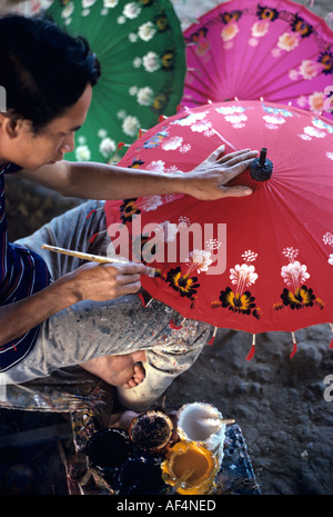 Skilled artist with black and yellow colours on one brush painting flowers on top of red umbrellas Bor Sang Village Thailand Stock Photo