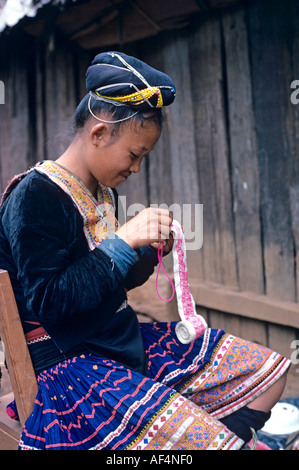 Side view portrait of a young Hmong or Meo Hill Tribal girl in traditional dress doing needlework Northern Thailand Stock Photo