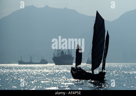 Traditional style Chinese sailing junk in late 1970’s on misty sea sun sparkling off water in Victoria Harbour Hong Kong China Stock Photo