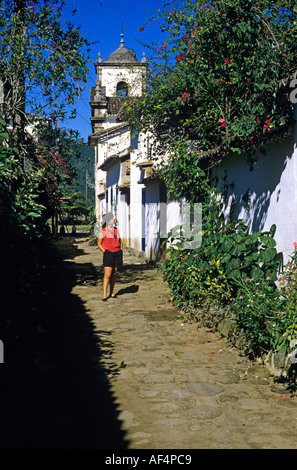 Local girl walks on old cobbled street with greenery and white walls in Parati on the Costa Verde Rio de Janeiro State Brazil Stock Photo