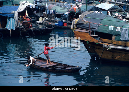 Two small children on a small traditional junk one holding the stern paddle in Causeway Bay typhoon shelter Hong Kong China Stock Photo