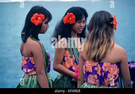 Side back view portrait of three lovely local dark skinned girl Hawaiian dancers in blue and red flowered blouses Hawaii Stock Photo