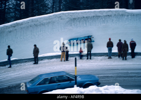 People watch two man toboggan bank hard round a vertical curve on the Cresta Run at St Moritz The Engadin Switzerland Stock Photo