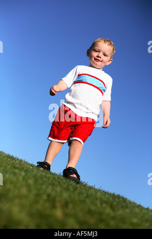 Two year old boy walking on grass with bright blue sky. Stock Photo