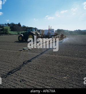 John Deere tractor & trailed sprayer spraying very young spring field bean crop Stock Photo