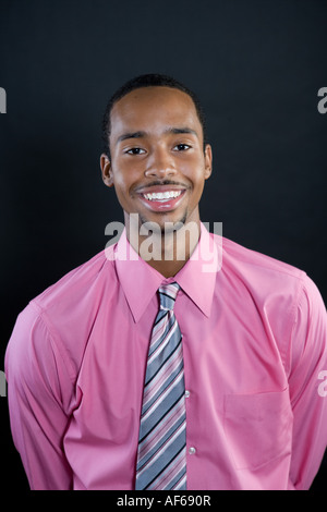 Portrait of a young smiling 18 year old African American man wearing a pink shirt and striped tie