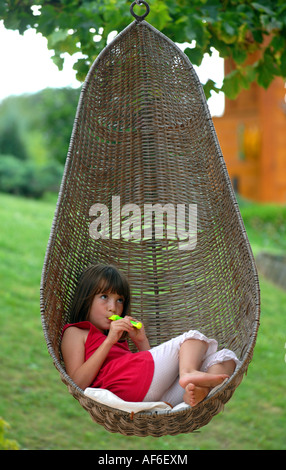 Hanging wicker basket chair, girl using hanging basket chair and playing flute Stock Photo