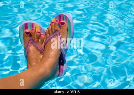 Horizontal close up of a woman's tanned feet with painted toenails wearing striped flip flops against a blue swimming pool Stock Photo