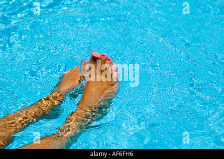 Horizontal close up of tanned wet feet with painted toenails splashing around in a bright blue pool Stock Photo