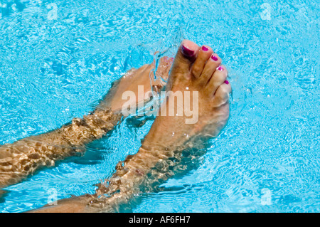 Horizontal close up of tanned wet feet with painted toenails splashing around in a bright blue pool Stock Photo