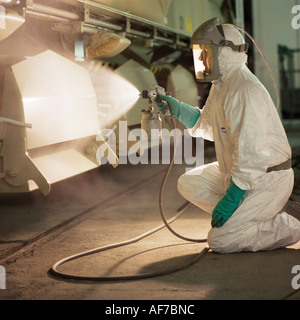Man in protective clothing spray painting side of locomotive railway carriage. Stock Photo