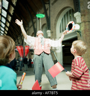Street entertainer balancing act with two children watching in covered town centre old building plaza. Stock Photo