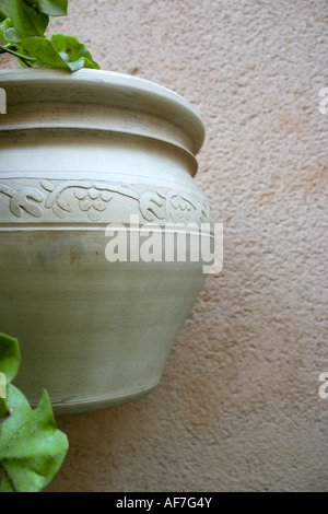 Unglazed white pot holding a bit of greenery hangs against a rough exterior stucco wall. Stock Photo