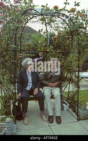 elderly couple enjoying a relaxing sit under a rose arbour in a garden in West Sussex Stock Photo