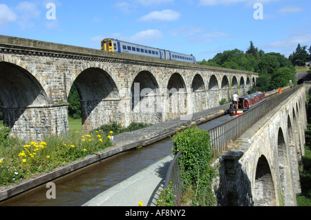 A  narrow boat on Llangollen Canal passes over Chirk Aqueduct with a train on the viaduct Stock Photo