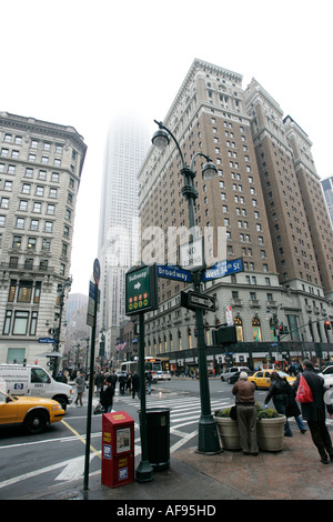 pedestrians walking across road at busy traffic junction of west 34th street st and broadway with empire state building misty Stock Photo