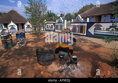 South Africa Mapoch Ndebele Village near Pretoria Woman cooking Houses with traditional wall paintings in background. Stock Photo