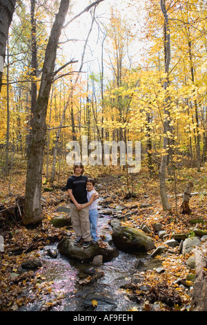 Two boys pose for a photo standing on rocks in stream surrounded by fall colors in a late autumn forest .Model Released