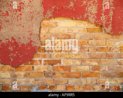 Painted red cement flaking off of an orange and yellow brick wall Stock Photo