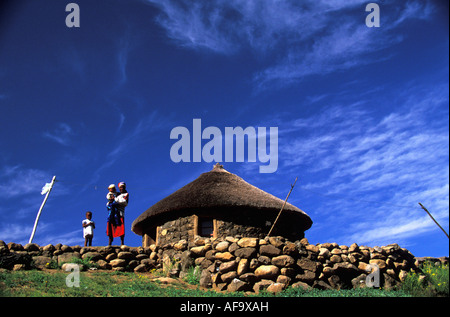 A woman standing outside her neat stone and thatch homestead with her children. Lesotho Stock Photo