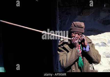 Portrait of old Sotho man leaning against the wall of a stone building, playing traditional wind instrument. Stock Photo