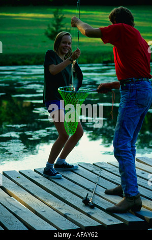 Dad helps daughter net a bass from her rod at farm pond MR Stock Photo