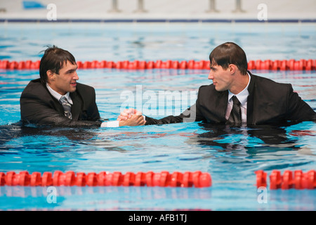 Wet businessmen shaking hands in pool Stock Photo