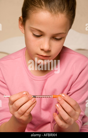 Young girl prepares her insulin injection to help battle her diabetes. Young girl played by a model. Stock Photo