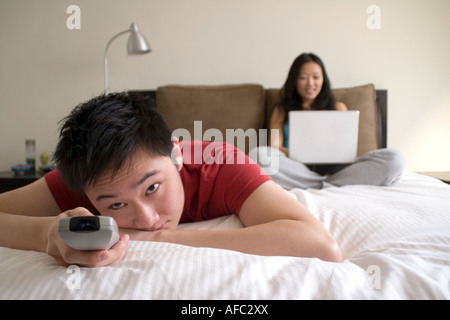 Man Watching Television, Woman Working on Laptop in Background Stock Photo