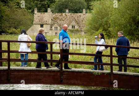 Tourists on bridge over River Coln Bibury Cotswolds Gloucestershire England UK Arlington Row in background Stock Photo