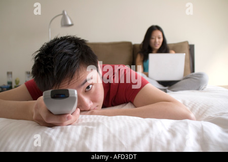 Man Watching Television, Woman Working on Laptop in Background Stock Photo