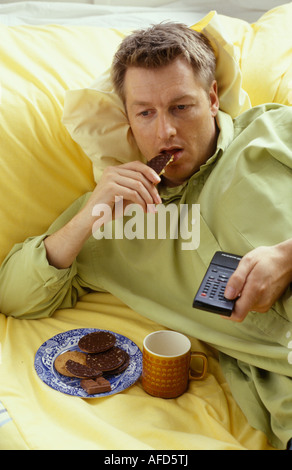 man eating biscuits and drinking tea in front of the television Stock Photo
