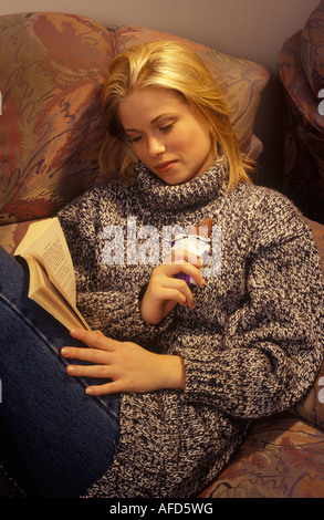 woman curled up with a book eating a bar of chocolate Stock Photo