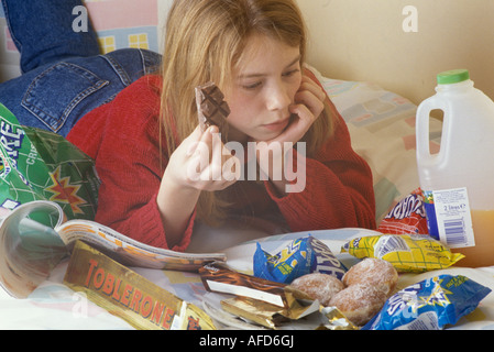 girl binge eating while reading a magazine Stock Photo