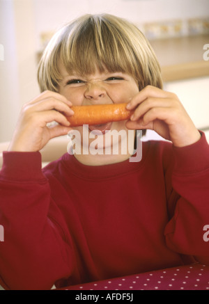 Young boy sitting in a kitchen with a carrot - having fun Stock Photo