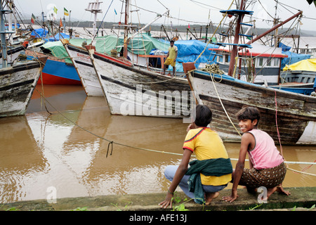 Young local lads crouching next to fishing boats on mooring on Zuari River in Cortalim Marmugao district Goa India Asia Stock Photo