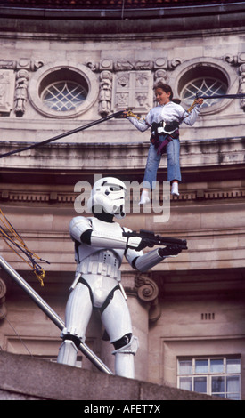 Little girl jumping on bungy cord looking down on a Star Wars Storm Trooper before London County Hall, South Bank, London Stock Photo