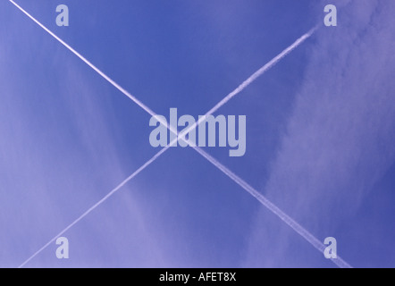 Two white jet vapour trails forming an X against a blue sky Stock Photo