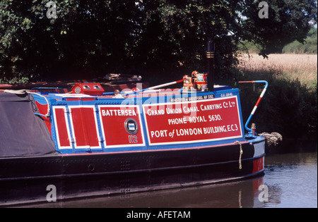 Brightly painted traditional working narrowboat (Grand Union Canal Carrying Co) with striped tiller and canalware, Staffordshire Stock Photo