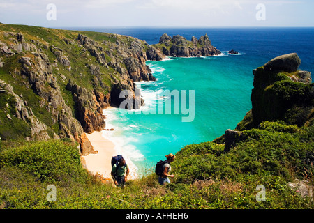 Young man and woman climb up cliff from Pedn Vounder Pednvounder beach with Treen Cliffs Logan's Logans Rock Cornwall England Stock Photo