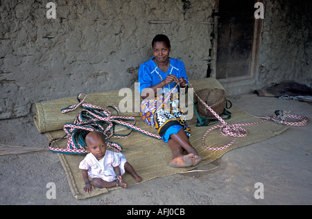 AFRICA KENYA DIGO Kenyan mother keeps an eye on her baby girl while she weaves a ribbon to trim her straw mat Stock Photo