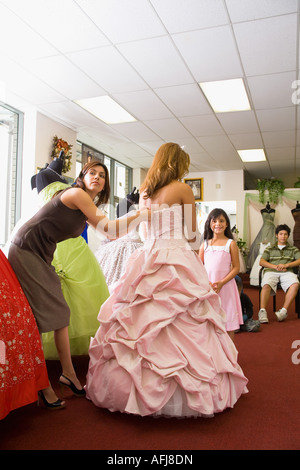 Salesgirl zips up teenage girl's party dress, little sister looks on Stock Photo