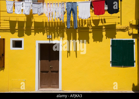 Laundry hangs from clothesline above door of yellow house Burano Italy Stock Photo