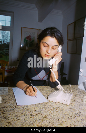 Young Woman Answering Phone At Home Taking Message Stock Photo