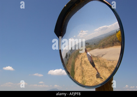 traffice mirror relecting a man standing along a country road on the Regaliali winery estate in Sicily Italy on a sunny day Stock Photo