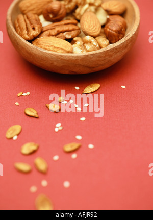 Mixed nuts and seeds in wooden bowl on bright red background Stock Photo