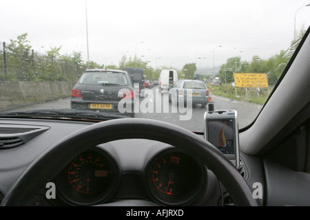 dashboard and steering wheel of car stuck in traffic on rainy day using PDA sat nav on westlink Stock Photo