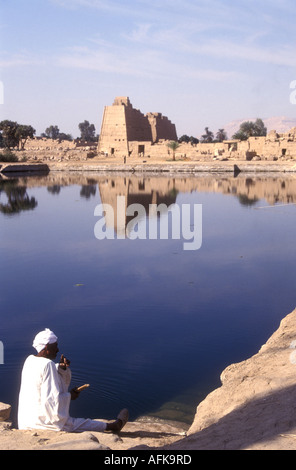 An Egyptian in traditional dress sitting on the bank of the Sacred Lake of the Temple of Karnak near Luxor Egypt Stock Photo